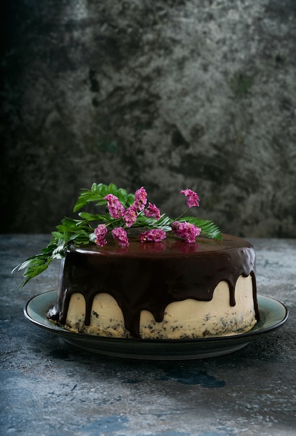 Pastel de chocolate casero con capas de crema de mantequilla de maní decorado con flores en la parte superior sobre un escritorio rústico oscuro. Vista lateral.