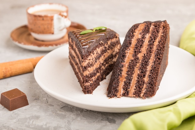 Pastel de chocolate casero con crema de leche y una taza de café sobre una superficie de hormigón gris. Vista lateral, enfoque selectivo.