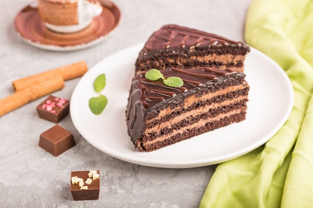 Pastel de chocolate casero con crema de leche y una taza de café sobre una superficie de hormigón gris. Vista lateral, enfoque selectivo.