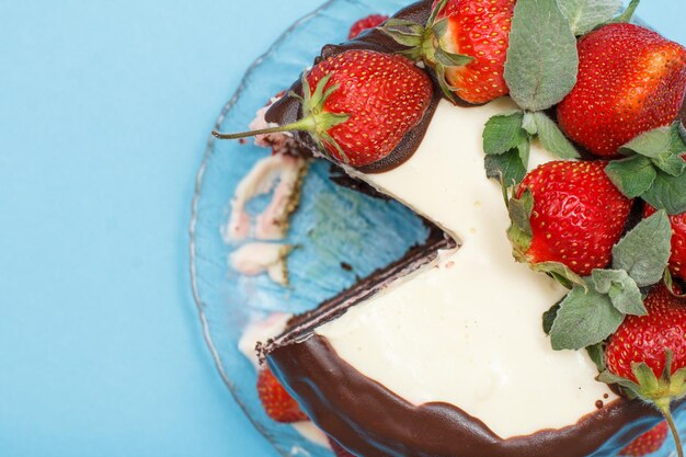 Pastel de chocolate casero decorado con fresas frescas en una placa de vidrio sobre el fondo azul.