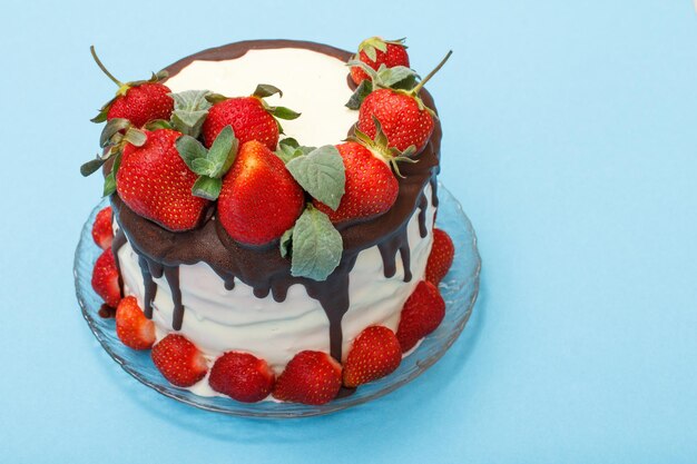 Pastel de chocolate casero decorado con fresas frescas en placa de vidrio sobre fondo de color azul