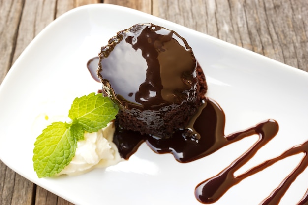 Pastel de chocolate con crema batida en el plato blanco. Sobre la mesa de madera.