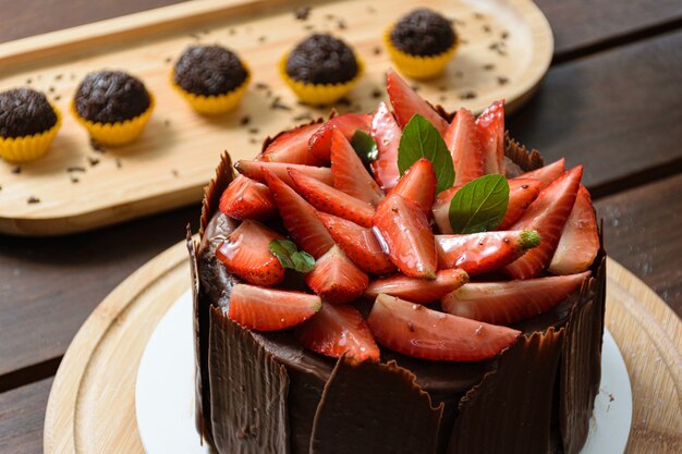 Pastel de chocolate cubierto de fresas, hojas de albahaca, mermelada de moras y con platos de chocolate alrededor. Al fondo brigadier (dulce brasileño).