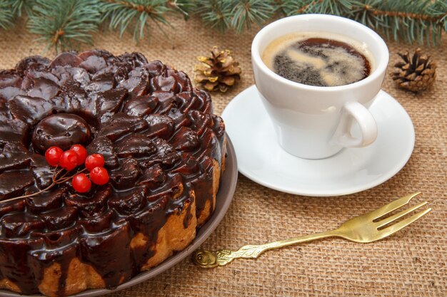 Pastel de chocolate decorado con manojo de viburnum, taza de café en la mesa con rama de abeto, tenedor y cilicio.