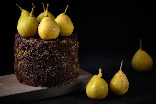 Pastel de chocolate decorado con pistachos molidos y peras frescas sobre una tabla de madera.