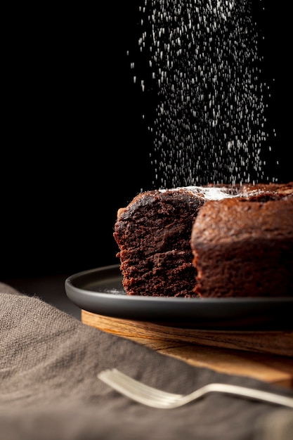 Foto pastel de chocolate espolvoreado con azúcar en polvo sobre una placa negra