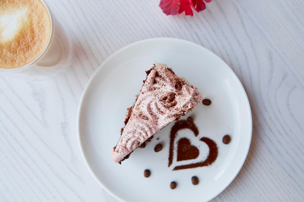 Pastel de chocolate con frutas estéticas y un vaso con doble fondo de café con leche en una mesa de madera al aire libre Decoraciones de flores rosas en la terraza del café Desayuno atmosférico Vista superior