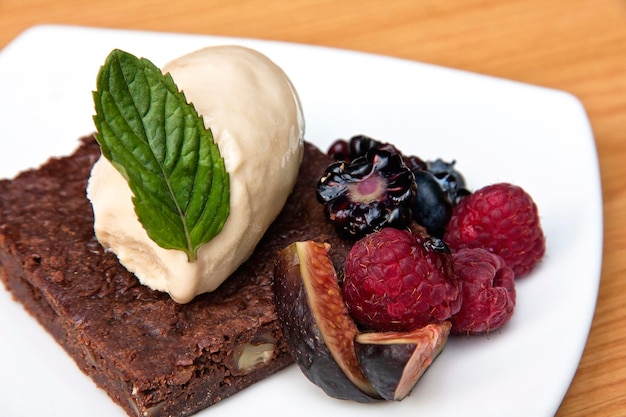 Pastel de chocolate con helado de nuez, bayas rojas e higos servidos en un plato blanco sobre fondo de madera