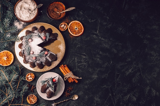 Pastel de chocolate navideño decorado con bayas y romero sobre un fondo negro, vista superior, gratis