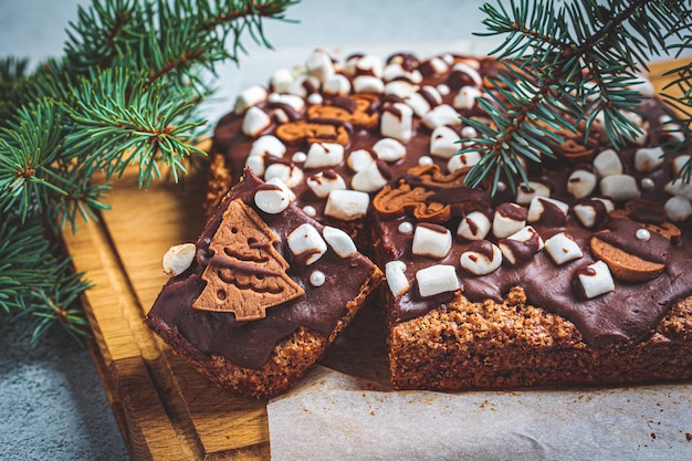 Pastel de chocolate navideño decorado con malvaviscos, galletas de jengibre y chocolate en una tabla de madera Concepto de postre navideño