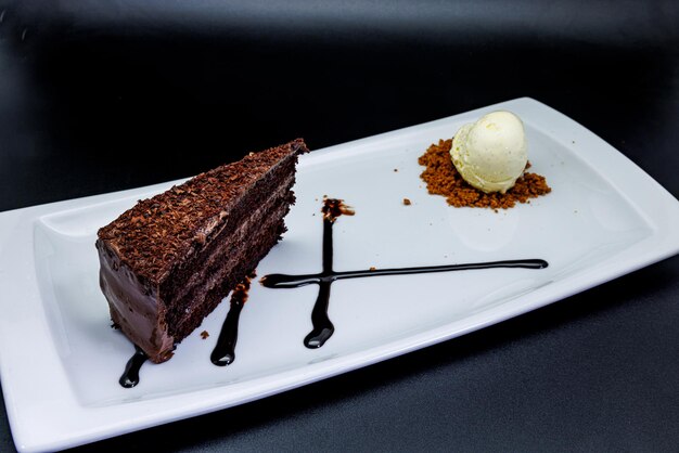 Pastel de chocolate en un plato blanco con helado sobre un fondo blanco.