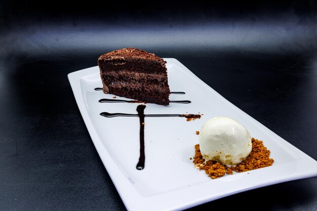 Pastel de chocolate en un plato blanco con helado sobre fondo negro