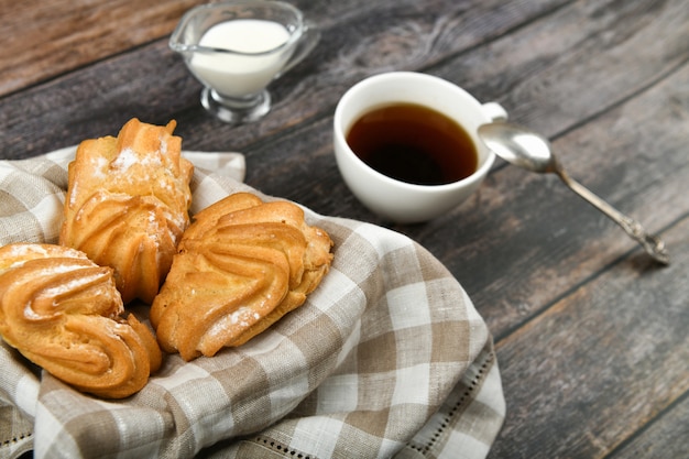 Pastel de choux con café en una madera. En una cesta sobre una toalla a cuadros. . Chic con requesón. Pequeños pasteles de crema en un recipiente de mimbre en madera