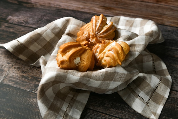 Pastel de choux en madera. En una cesta sobre una toalla a cuadros. El departamento estaba mintiendo. . Chic con requesón. Pequeños pasteles de crema en un recipiente de mimbre en madera