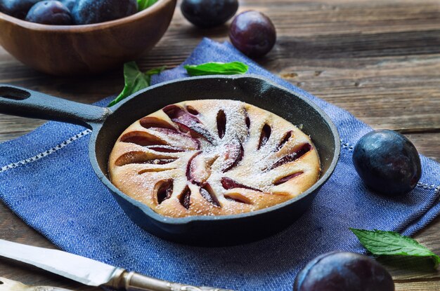 Pastel de ciruela casera fresca en una sartén de hierro sobre fondo de madera rústica.