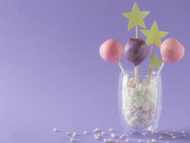 Pastel de color pastel aparece en un vaso con malvaviscos y chispitas. Postre festivo de cumpleaños. pared violeta imagen horizontal lugar para el texto