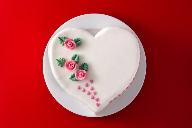 Pastel de corazón para el día de San Valentín, el día de la madre o el cumpleaños, decorado con rosas y corazones de azúcar rosa sobre fondo rojo.