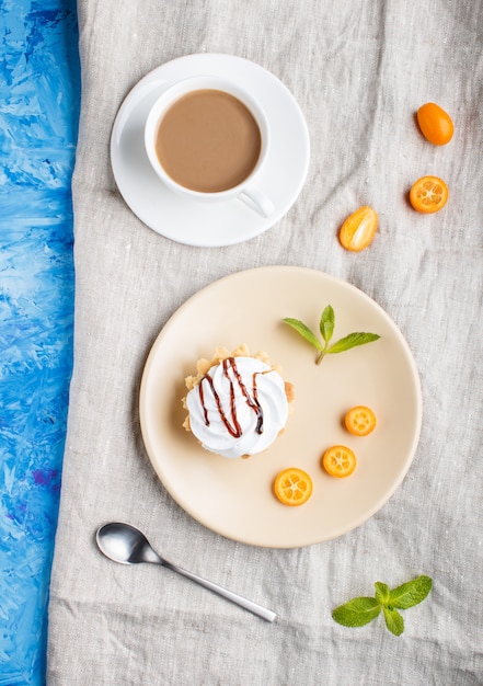 Pastel con crema batida de huevo en un plato de color marrón claro con rodajas de kumquat y hojas de menta en un cemento azul. vista superior.