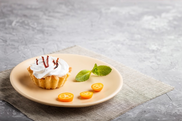 Pastel con crema batida de huevo en un plato marrón claro con rodajas de kumquat y hojas de menta