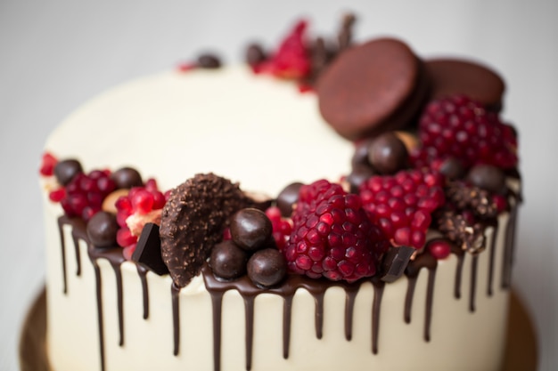 Pastel con crema blanca, gotas de chocolate, granada, nueces y decoración de chocolate