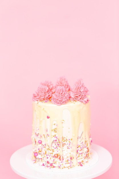 Pastel de crema de mantequilla rosa y blanco con chispas rosadas y goteo de ganache de chocolate blanco.