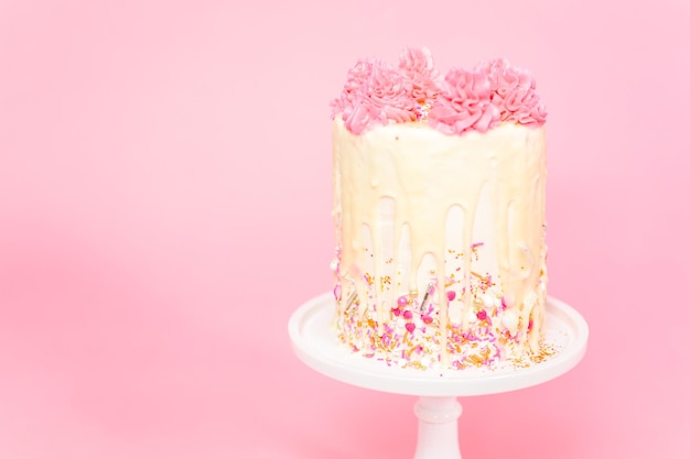 Foto pastel de crema de mantequilla rosa y blanco con chispas rosadas y goteo de ganache de chocolate blanco.
