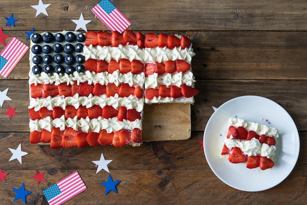 Pastel cuadrado con los colores de la bandera estadounidense sobre un fondo de madera con decoración Plato con rebanada de pastel Celebración del Día de la Independencia