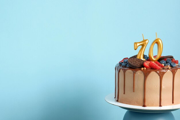 Pastel de cumpleaños de chocolate con galletas de bayas y número setenta velas doradas en el espacio de copia de fondo de pared azul