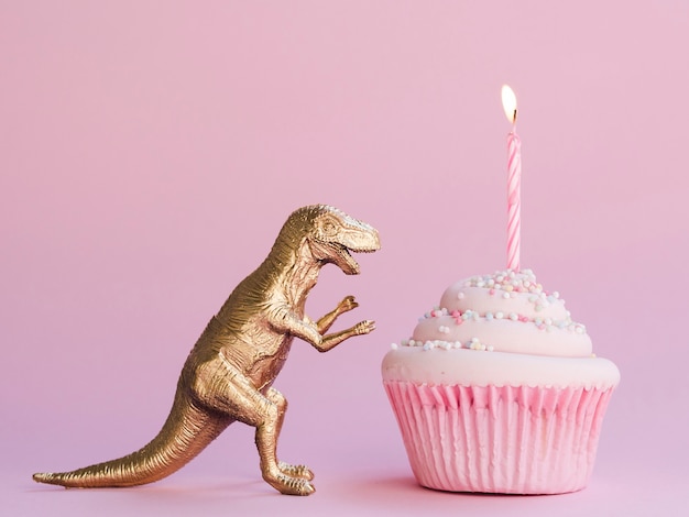 Pastel de cumpleaños y dinosaurio divertido sobre fondo rosa