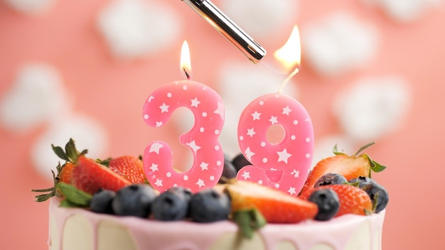 Pastel de cumpleaños número 39 vela rosa en un hermoso pastel con bayas y encendedor con fuego contra el fondo de nubes blancas y cielo rosa Vista de cerca