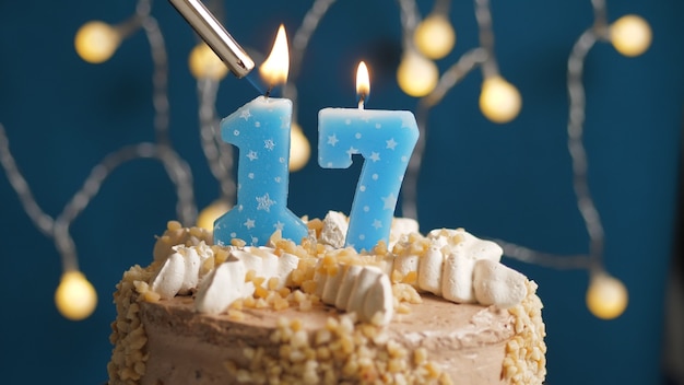 Pastel de cumpleaños con vela número 17 en backgraund azul prendido fuego por encendedor. De cerca