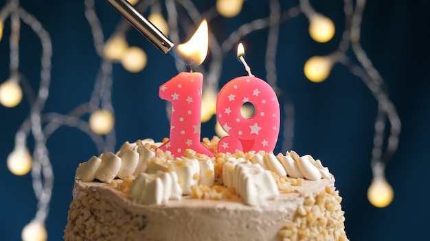 Pastel de cumpleaños con vela rosa número 19 en backgraund azul prendido fuego por encendedor. Vista de primer plano