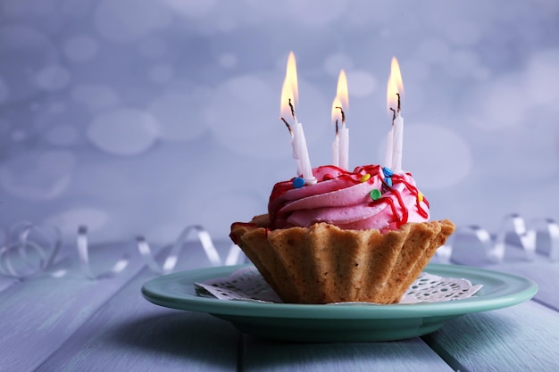 Pastel de cumpleaños con velas en un plato sobre una mesa de madera de color y fondo claro