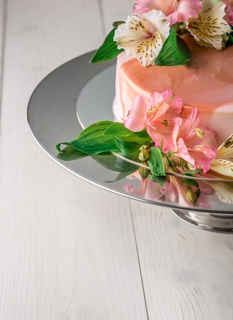 Pastel decorado con flores. Pastel de boda en un soporte sobre un fondo de madera blanca