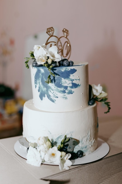 Un pastel de dos niveles con flores azules y un pastel blanco con el número 60.