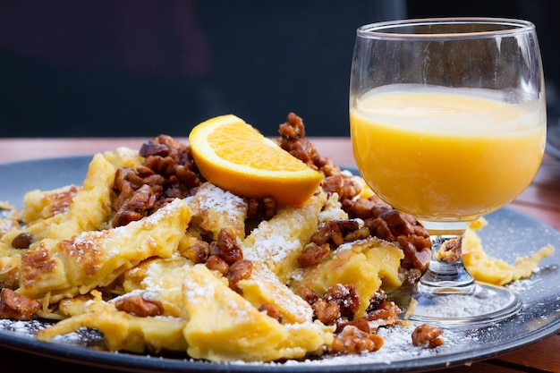 Pastel dulce con nueces, pasas, azúcar en polvo, rodaja de naranja encima y vaso de licor de crema