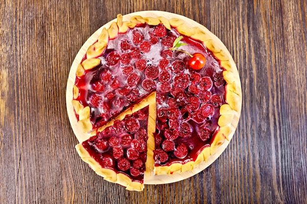 Pastel dulce redondo con cerezas y mermelada sobre un fondo de tablas de madera