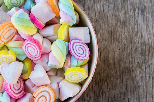 Pastel e colorfu de marshmallow e gomosos em uma tigela de madeira na mesa de madeira.