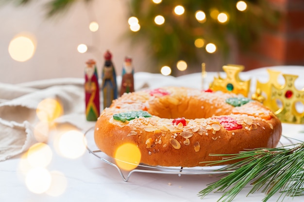 Pastel de Epifanía tradicional español, Roscon de Reyes con tres reyes, corona, adornos festivos y luces navideñas