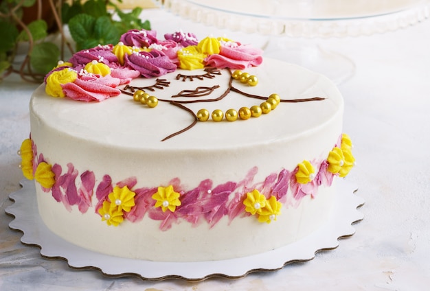 Pastel festivo con flores de color crema y una carita de niña sobre un fondo claro