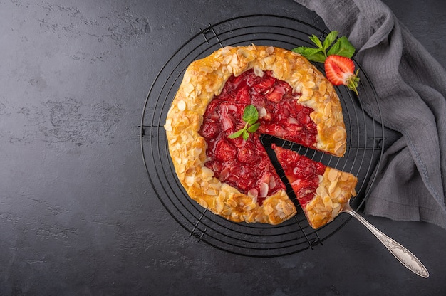 Pastel de flan casero con fresas, menta y pétalos de almendra con un trozo cortado en la espátula