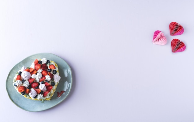 Pastel en forma de corazón decorado con frutos rojos y merengue. Fondo blanco. Día de San Valentín. Copie el espacio.