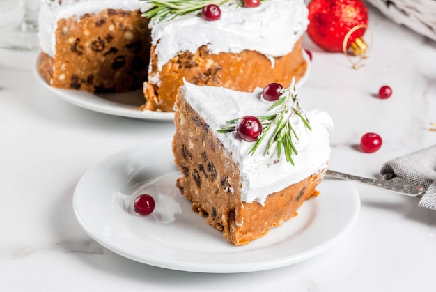 Pastel de fruta de Navidad o pudín, decorado con romero y arándano, con decoración navideña, en mesa de mármol blanco, espacio de copia