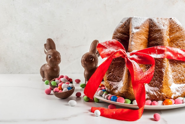 Pastel de fruta tradicional italiana Panettone Pandoro con cinta roja festiva, conejos de Pascua y decoraciones de huevos de caramelo dulce, en casa de madera,