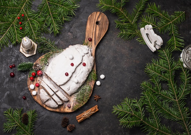 Pastel de frutas tradicional de Navidad sobre tabla de cortar de madera fondo rústico de madera negra con adornos navideños vista superior con espacio de copia