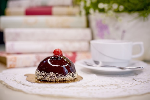 Foto pastel de glaseado de chocolate con té sobre una mesa con flores y libros.