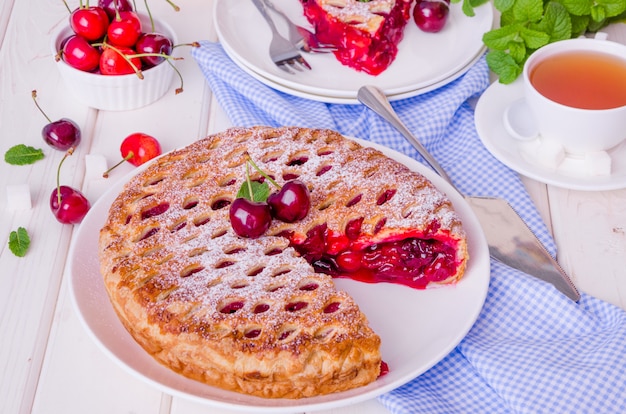 Pastel de hojaldre cerrado con cereza relleno sobre un fondo blanco de madera.