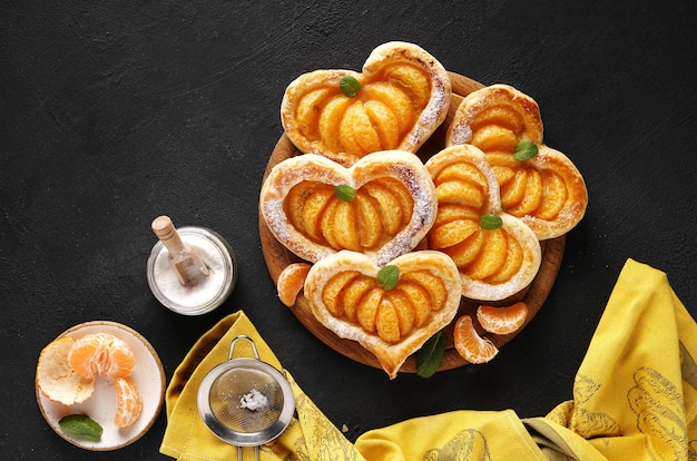 Pastel de hojaldre en forma de corazón con rodajas de mandarina sobre una tabla de madera sobre una mesa oscura con