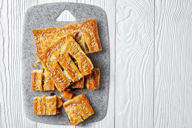 Foto pastel de hojaldre de verduras americano con queso de cabra cubierto con semillas de girasol y sésamo relleno de verduras asadas servido sobre un fondo de madera blanca, vista superior, primer plano