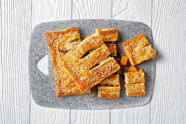 Pastel de hojaldre de verduras americano con queso de cabra cubierto con semillas de girasol y sésamo relleno de verduras asadas servido sobre un fondo de madera blanca, vista superior, primer plano